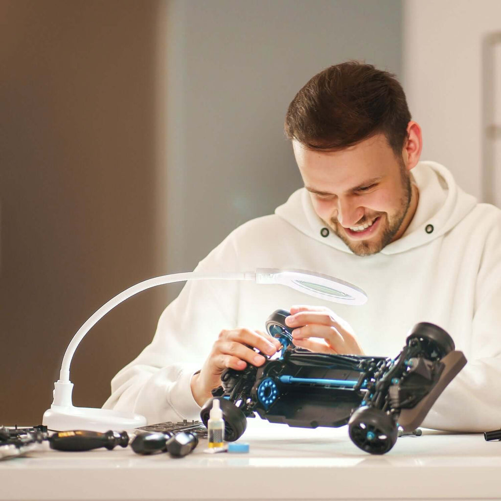Homme utilisant une lampe-loupe LED Lumeno 680X pour assembler une maquette de voiture, illustrant l'éclairage LED puissant pour les travaux de détail.